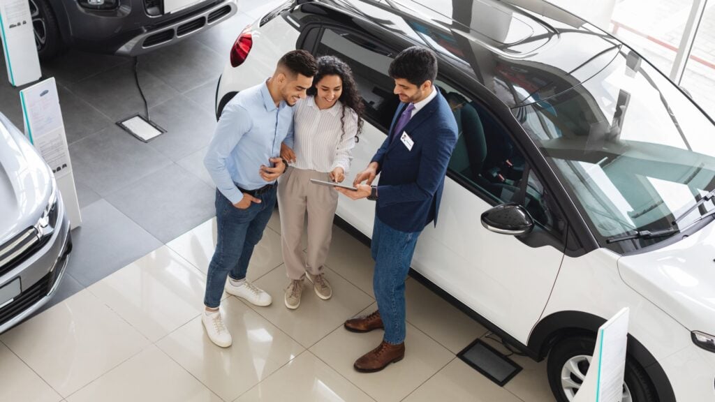 Car Sales Top view of wealthy middle eastern young couple having conversation with male sales assistant at luxury auto showroom