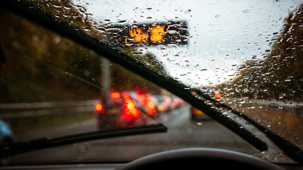 Wipers clearing rain, and roads busy with traffic as the light fades on a winter commute.